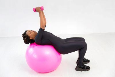 A person lying on a pink ball with a pink dumbbell

Description automatically generated